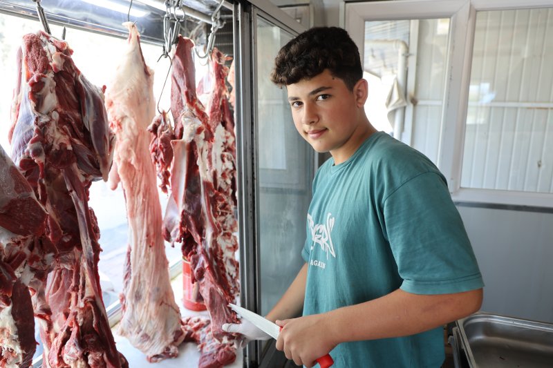 6 yıldır babasının yanında mesleği öğrenen 14 yaşındaki kasap, yılların ustalarına meydan okuyor (Fotoğraflı) Ramazan İlın HATAY (İHA) - Hatay'da yaşıtlarının aksine telefonla oyun oynamak yerine aile mesleği kasaplığını öğrenen 14 yaşındaki Muhammed Enes Başak, usta elleriyle eşsiz tatlara lezzet veriyor. Antakya ilçesi Esenlik Mahallesi'nde yaşayan 14 yaşındaki Muhammed Enes Başak, 8 yaşından beri kasaplık yapan babası Nuri Başak'ın yanında mesleğin inceliklerini öğreniyor. Babasına ait kasap dükkanında usanmadan, pes etmeden mesai yapan kasap Başak; babasından öğrendiği mesleğinde kendini geliştirmeye devam ediyor. İş yerine gelen müşterilerin özel istekte bulunduğu Muhammed Enes Usta; hayvan kesimi gerçekleştirirken Hatay’ın eşsiz lezzetleri olan kağıt kebabı, tepsi kebabı ve lahmacun gibi yemekleri yapabiliyor. Okul zamanlarında okula giden Muhammed Enes Usta, okul sonrası çoğu zamanını babasının yanında çalışarak geçiriyor. Ailede gelenek haline gelmiş kasaplık mesleğini devam ettiren Muhammed Enes Usta, ilerideki hedefi babasının işlerini daha da ileriye taşımak ve çok daha güzel hale getirmek. Aile mesleği olan kasaplığı severek yapan Muhammed Enes Usta, mesleğinde olan yeteneğiyle yılların kasap ustalarına meydan okuyor. “Okul zamanında okula gidiyorum ve boş zamanlarımda babamın yanına gelip mesleği öğreniyorum” Kasaplık mesleğinin ailenin geleneği olduğunu ve bu geleneği devam ettirmek istediğini belirten 14 yaşındaki kasap Muhammed Enes Başak, “14 yaşındayım ve 8. sınıf öğrencisiyim. Etleri kesip kıyma makinesini atıyoruz. Maydanozla birlikte harç yaptıktan sonra tepsi kebabı ve kağıt kebabı yapıyoruz. Fırınlarda pişirip müşterilere hizmet ediyoruz. 8 yaşından dedem ilk bana öğretti, babam ise beni kasap dükkanı getirip götürürdü. Bu kasap mesleğine yavaş yavaş öğrenmeye başladım. Dedemden, babamdan da bana geçen bu geleneği devam ettireceğim. Ben bu mesleği sevdiğim için burada çalışıyorum. Yaz tatilinde kesimhaneye gidiyorum. Burada mesleğin daha iyi inceliklerini öğreniyorum. Dana, inek ve koyunları kesip onların etlerini ayırıyoruz. Babamın açtığı iş yerini daha iyi ve daha güzel bir hale getirmek istiyorum. Okul zamanında okula gidiyorum ve boş zamanlarımda babamın yanına gelip mesleği öğreniyorum. Kasap mesleğini tam öğrenmiş olduğum için müşterilerin bazıları sen yap dedikleri için ben de onları yapıp onlara veriyorum” dedi. “Bazı müşterimiz geliyor, ‘Enes bana kağıt kebabı yap veya tepsi kebabı yap’ diyorlar” Evladının okulundan geriye kalan zamanlarda kendisine yardım ederek mesleği öğrendiğini ve kendine özel müşterileri olduğunu belirten baba Nuri Başak, “Kendisini ilk başta bu mesleği sevmesi gerekiyor. Dedesinden dolayı bu mesleği çok seviyor. Bu işi yapmaya karar verdi ve bu işi severek yapıyor. Her mesleğin kendine göre zorluğu var. Severek yapılan bir meslekte zorluk olmaz. 8 yaşından beri boş zamanlarda yanıma geliyor. Tepsi kebabı, kağıt kebabı, lahmacun, kuşbaşı ve kıyma gibi ne isterse yapar. Rahmetli dedemden babama babamdan bana benden de çocuğuma kalacak. Müşterilerim oğlumdan çok memnun oluyor. Özellikle bazı müşteriler oğlumun yapmasını istiyorlar. Benim elimin lezzeti oğluma geçmiş. Bazı müşterimiz geliyor, ‘Enes bana kağıt kebabı yap veya tepsi kebabı yap’ diyorlar. Oğlum da istediklerini yapıyor. Oğlumun müşteri potansiyeli benden daha iyi oldu. Oğlumu bu işi severek yaptığı için ileride daha başarılı daha güzel bir mekan açıp kendi işini kuracağına inanıyorum” ifadelerini kullandı.