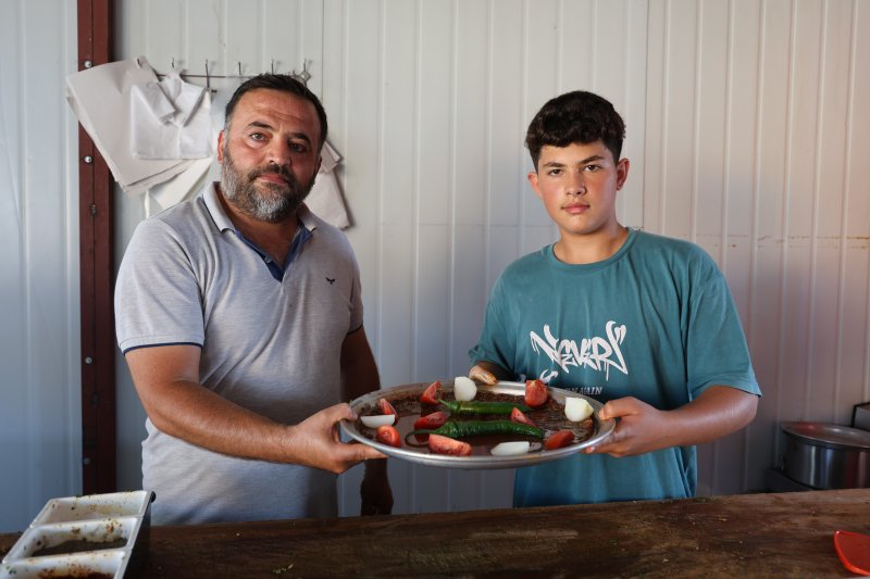 6 yıldır babasının yanında mesleği öğrenen 14 yaşındaki kasap, yılların ustalarına meydan okuyor (Fotoğraflı) Ramazan İlın HATAY (İHA) - Hatay'da yaşıtlarının aksine telefonla oyun oynamak yerine aile mesleği kasaplığını öğrenen 14 yaşındaki Muhammed Enes Başak, usta elleriyle eşsiz tatlara lezzet veriyor. Antakya ilçesi Esenlik Mahallesi'nde yaşayan 14 yaşındaki Muhammed Enes Başak, 8 yaşından beri kasaplık yapan babası Nuri Başak'ın yanında mesleğin inceliklerini öğreniyor. Babasına ait kasap dükkanında usanmadan, pes etmeden mesai yapan kasap Başak; babasından öğrendiği mesleğinde kendini geliştirmeye devam ediyor. İş yerine gelen müşterilerin özel istekte bulunduğu Muhammed Enes Usta; hayvan kesimi gerçekleştirirken Hatay’ın eşsiz lezzetleri olan kağıt kebabı, tepsi kebabı ve lahmacun gibi yemekleri yapabiliyor. Okul zamanlarında okula giden Muhammed Enes Usta, okul sonrası çoğu zamanını babasının yanında çalışarak geçiriyor. Ailede gelenek haline gelmiş kasaplık mesleğini devam ettiren Muhammed Enes Usta, ilerideki hedefi babasının işlerini daha da ileriye taşımak ve çok daha güzel hale getirmek. Aile mesleği olan kasaplığı severek yapan Muhammed Enes Usta, mesleğinde olan yeteneğiyle yılların kasap ustalarına meydan okuyor. “Okul zamanında okula gidiyorum ve boş zamanlarımda babamın yanına gelip mesleği öğreniyorum” Kasaplık mesleğinin ailenin geleneği olduğunu ve bu geleneği devam ettirmek istediğini belirten 14 yaşındaki kasap Muhammed Enes Başak, “14 yaşındayım ve 8. sınıf öğrencisiyim. Etleri kesip kıyma makinesini atıyoruz. Maydanozla birlikte harç yaptıktan sonra tepsi kebabı ve kağıt kebabı yapıyoruz. Fırınlarda pişirip müşterilere hizmet ediyoruz. 8 yaşından dedem ilk bana öğretti, babam ise beni kasap dükkanı getirip götürürdü. Bu kasap mesleğine yavaş yavaş öğrenmeye başladım. Dedemden, babamdan da bana geçen bu geleneği devam ettireceğim. Ben bu mesleği sevdiğim için burada çalışıyorum. Yaz tatilinde kesimhaneye gidiyorum. Burada mesleğin daha iyi inceliklerini öğreniyorum. Dana, inek ve koyunları kesip onların etlerini ayırıyoruz. Babamın açtığı iş yerini daha iyi ve daha güzel bir hale getirmek istiyorum. Okul zamanında okula gidiyorum ve boş zamanlarımda babamın yanına gelip mesleği öğreniyorum. Kasap mesleğini tam öğrenmiş olduğum için müşterilerin bazıları sen yap dedikleri için ben de onları yapıp onlara veriyorum” dedi. “Bazı müşterimiz geliyor, ‘Enes bana kağıt kebabı yap veya tepsi kebabı yap’ diyorlar” Evladının okulundan geriye kalan zamanlarda kendisine yardım ederek mesleği öğrendiğini ve kendine özel müşterileri olduğunu belirten baba Nuri Başak, “Kendisini ilk başta bu mesleği sevmesi gerekiyor. Dedesinden dolayı bu mesleği çok seviyor. Bu işi yapmaya karar verdi ve bu işi severek yapıyor. Her mesleğin kendine göre zorluğu var. Severek yapılan bir meslekte zorluk olmaz. 8 yaşından beri boş zamanlarda yanıma geliyor. Tepsi kebabı, kağıt kebabı, lahmacun, kuşbaşı ve kıyma gibi ne isterse yapar. Rahmetli dedemden babama babamdan bana benden de çocuğuma kalacak. Müşterilerim oğlumdan çok memnun oluyor. Özellikle bazı müşteriler oğlumun yapmasını istiyorlar. Benim elimin lezzeti oğluma geçmiş. Bazı müşterimiz geliyor, ‘Enes bana kağıt kebabı yap veya tepsi kebabı yap’ diyorlar. Oğlum da istediklerini yapıyor. Oğlumun müşteri potansiyeli benden daha iyi oldu. Oğlumu bu işi severek yaptığı için ileride daha başarılı daha güzel bir mekan açıp kendi işini kuracağına inanıyorum” ifadelerini kullandı.